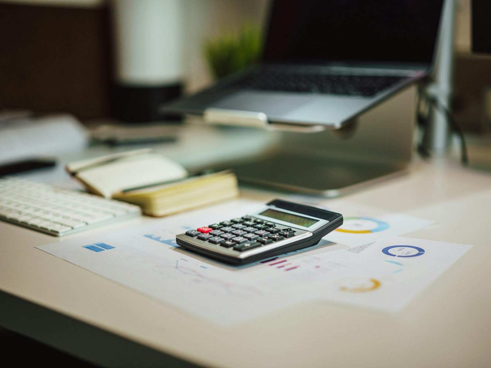 A desk with printed financial charts, a calculator and a laptop